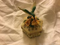 Hexagonal music box closed with ruby throated hummingbird perched on top of yellow flowers and green leaves