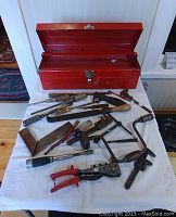 Photo of red metal tool box with open lid showing tray and antique hand tools spread out on cloth.