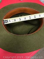 Top-down interior view of the green wool hat showing the brown leather inner band and approximate size measured by a tape from 0 to 6 inches.