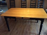 Full view of rectangular kitchen table with light wood top and black legs and frame