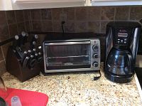 Photo showing the toaster oven, coffee maker, and knife block on granite countertop near wall outlet