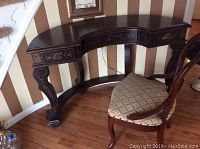 Full view of the half moon wooden desk with the upholstered chair beside it, showing hand painted detail on legs and drawer fronts.