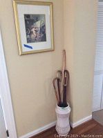 Photo of umbrella stand with canes inside and Cupid painting hanging above on wall.