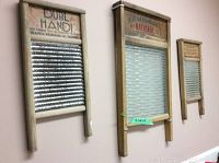 Three vintage wooden framed wash boards mounted on a pink wall, each with metal scrubbing surfaces of different sizes and different vintage labels.