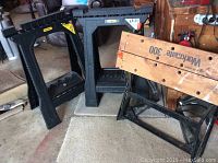 Three items including a Workmate 300 portable wooden top workbench with black metal frame and two black Stanley branded plastic sawhorses.