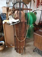 Full view of the vintage wooden King of the Hill sled with rope attached, alongside the hanging white ice skates.