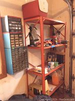 Full view of orange metal shelving with items on shelves and wall-mounted hardware organizer in garage