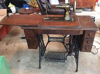 Full view of the antique Singer treadle sewing machine on wooden cabinet with seven drawers and treadle base
