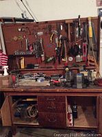 Full overview of wooden work bench with tools on pegboard and items on work surface, drawers and shelves below