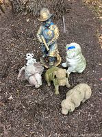 Overview of fireman statue, four dogs, and sitting angel placed on mulch ground outside under a tree