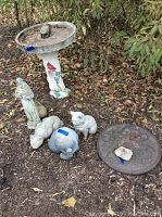 Wide shot showing all included garden statues, bird bath, and butterfly mat placed on soil bed with fallen leaves
