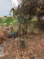 Full view of three-piece metal garden decor set standing outdoors amid fallen leaves and ornamental grasses. Shows size and outdoor placement.