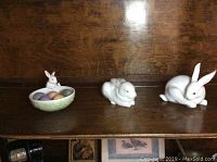 Front view of three Lladro bunny porcelain figurines including a small bunny dish with eggs and two bunny figures.