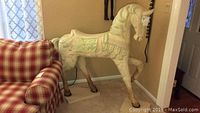 Front side of the large hand carved painted horse statue next to a chair for scale showing detailed carving and painting.