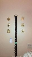 Photo of six brass horse brasses arranged on wall next to leather strap with bells