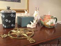 Photo showing dog treat canister, Lenox bunny figurines, oil and vinegar set, bunny teapot, Cordon Bleu bunny dish, Cracker Barrel mug, and brass compass wall art on wooden furniture.