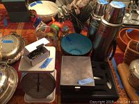 Photo showing vintage thermoses, a vintage scale, various ceramic figurines including a rooster, a blue decorative bowl, and containers with artificial flowers.