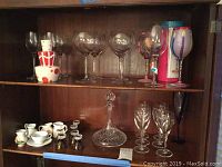 Wide view of shelf showing all items including wine glasses, decanter, mini pitchers, aperitif glasses, and teacup