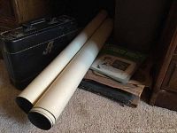 Black hard case with 'A' on outside, two rolled posters, stack of vinyl records on floor