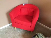 Red upholstered barrel chair with cushion, showing full chair in corner of room.