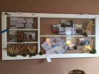 Full view of a large white distressed wood and glass door picture frame with photos and decorations inside.