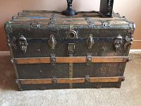 Front view of antique steamer trunk showing the worn textured surface, metal latches, and wooden reinforcements.