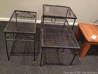 Three vintage wrought iron tables with mesh tops and decorative scrollwork on the sides, arranged on carpeted floor with a wooden table in background.