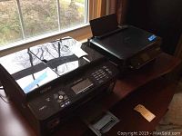Photo of Brother MFC-J825DW and Epson XP-410 printers on table near window.