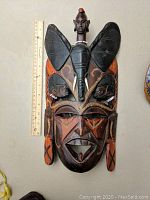 Front image of the wooden African mask showing detailed carvings, painted surfaces, beads, and leather straps on the back.
