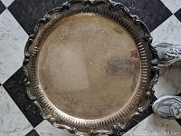 Top view of large round silver plated serving tray with tarnish and etched delicate pattern visible on surface and decorative edge detail.