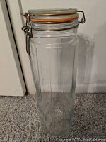 Tall clear glass canister with clamp-sealed lid and orange gasket sealing, approximately 12 inches high