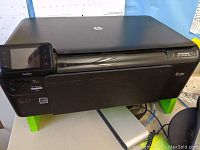 Front view of black HP Photosmart 5510 e-All-in-One printer with touchscreen and HP logo on top.