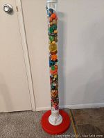 Full view of tall clear container filled tightly with various small rubber balls. Container has a white top and red base.
