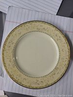 Top view of a Noritake Bone China dessert plate showing the cream border with gold floral pattern and gold rim.