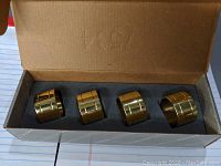 Open box showing 4 gold color polished brass napkin rings inside a foam insert for protection.
