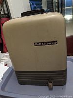 Beige rectangular carrying case with Bell & Howell logo on front.