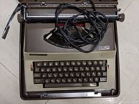 Front view of Royal electric typewriter with visible keyboard, carriage return arm, and power cord coiled on top.