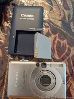 Canon PowerShot SD300 digital camera with battery charger and battery on patterned fabric background