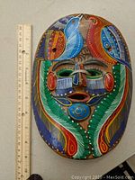Close-up photo of the ceramic mask showing colorful bird designs and ruler for size context.