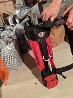 Red PAXX branded children's golf bag standing upright on concrete floor with multiple golf clubs inside.