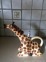 Photo side view of ceramic giraffe container showing brown spots, handle, and face with open mouth and textured mane.