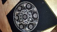 Top view photo of a round clear crystal platter displaying detailed cut-glass star and floral patterns with scalloped edges.