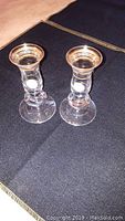 Two clear glass candle sticks with gold and platinum accents on a dark table with box partially visible