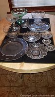 Photo showing a collection of assorted glassware including bowls, plates, and a small drinking glass arranged on a table with a dark cloth underlay.
