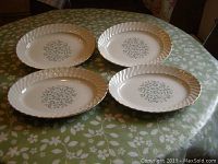 Set of four oval platters arranged on a table, each with leafy pattern in center and gold trimmed scalloped edges.