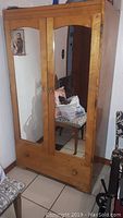 Front view of vintage wooden wardrobe with two doors, one mirrored, and a bottom drawer. Rounded wooden knobs on doors and drawer.