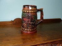 Photo showing one side of the stein depicting a rustic cabin and outdoor scene in relief.