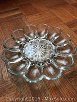 Photo of clear glass devilled egg serving dish on wood floor showing 12 individual compartments and decorative starburst center.