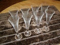 Eight clear crystal flute glasses arranged in two rows on a brown and beige patterned surface.