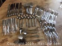 Overview of the full cutlery and serving utensils set, showing knives, forks, knives, spoons, butter knives, seafood forks, and serving utensils laid out on wooden surface.